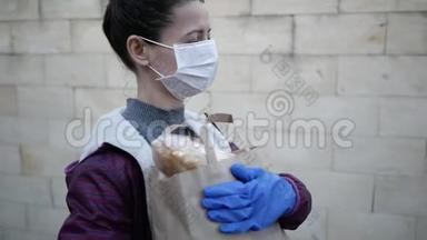 食品配送年轻妇女戴着防护面罩和手套，携带来自商店的产品。 流行病